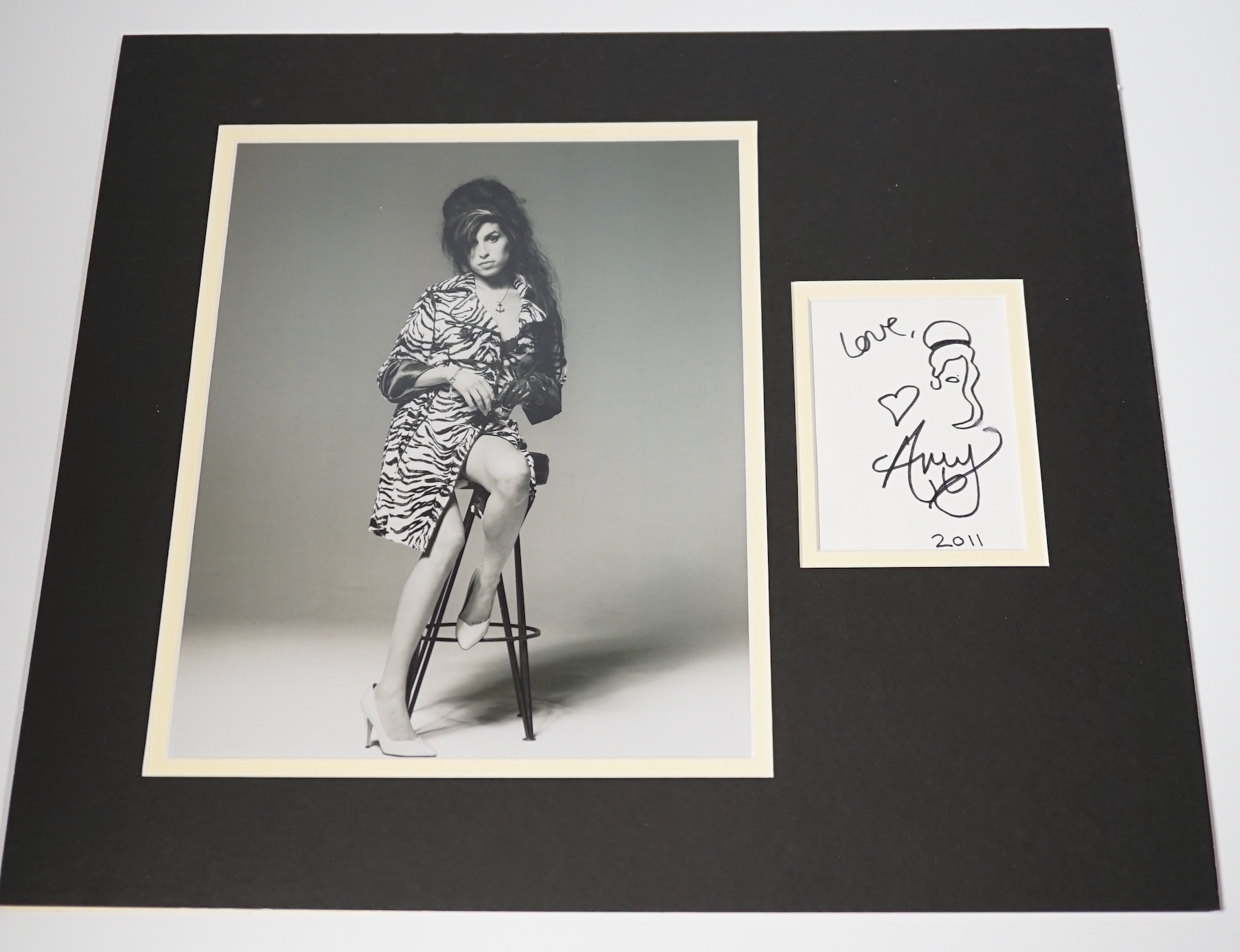 Amy Winehouse, an autograph with caricature self portrait dated 2011, mounted with a black and white portrait photograph